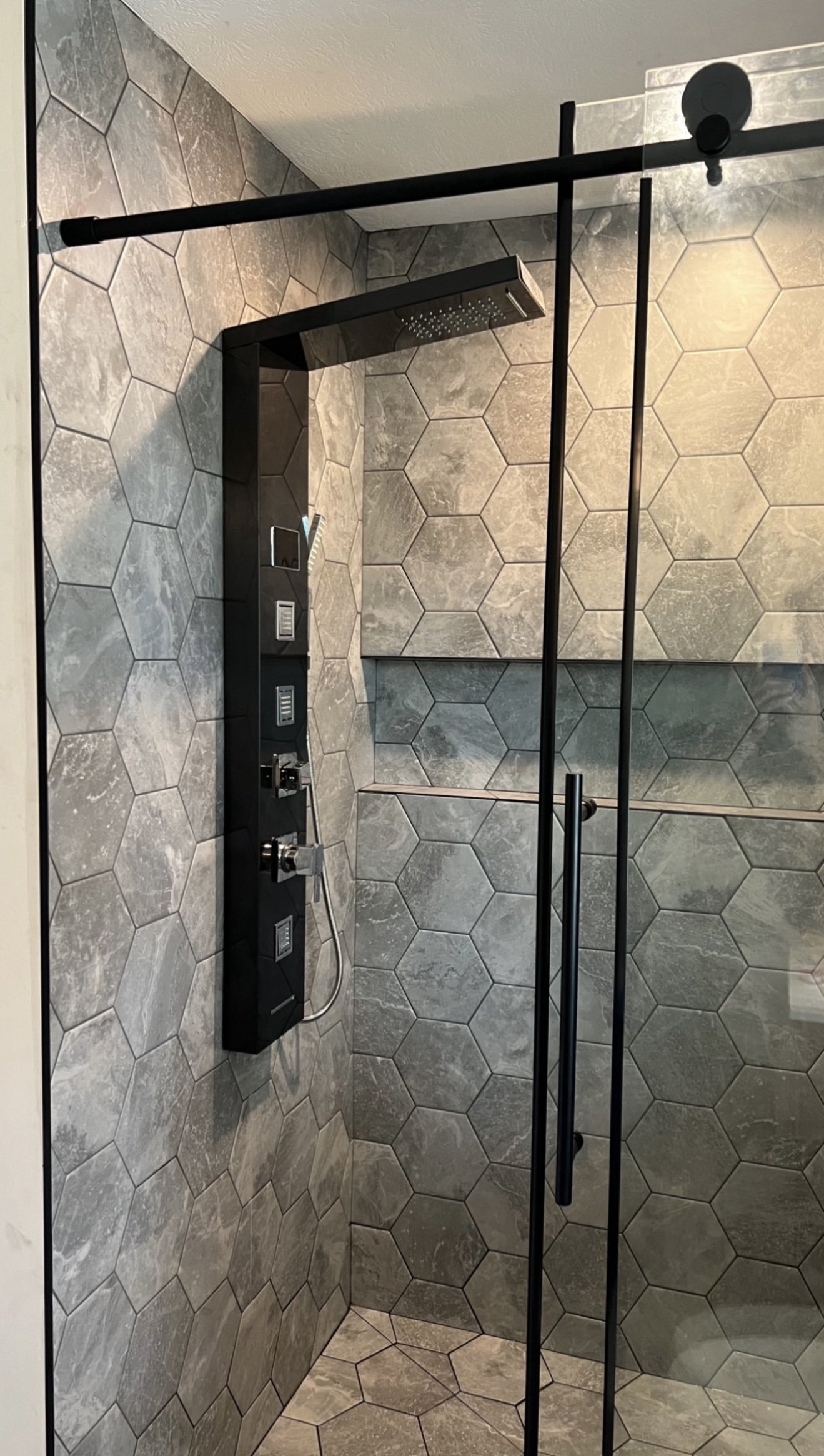 Modern shower with hexagonal gray tiles, black metal frame, and a rainfall showerhead.