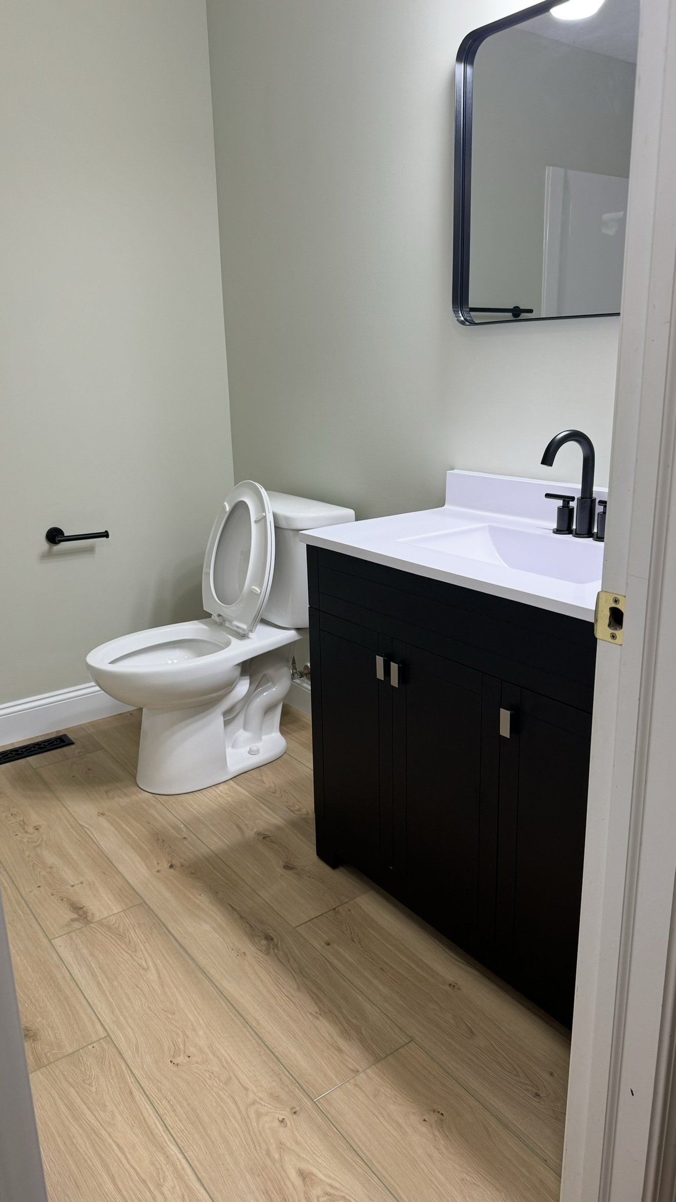 Modern bathroom interior with a white toilet, black vanity with sink, mirror, and light wood flooring.