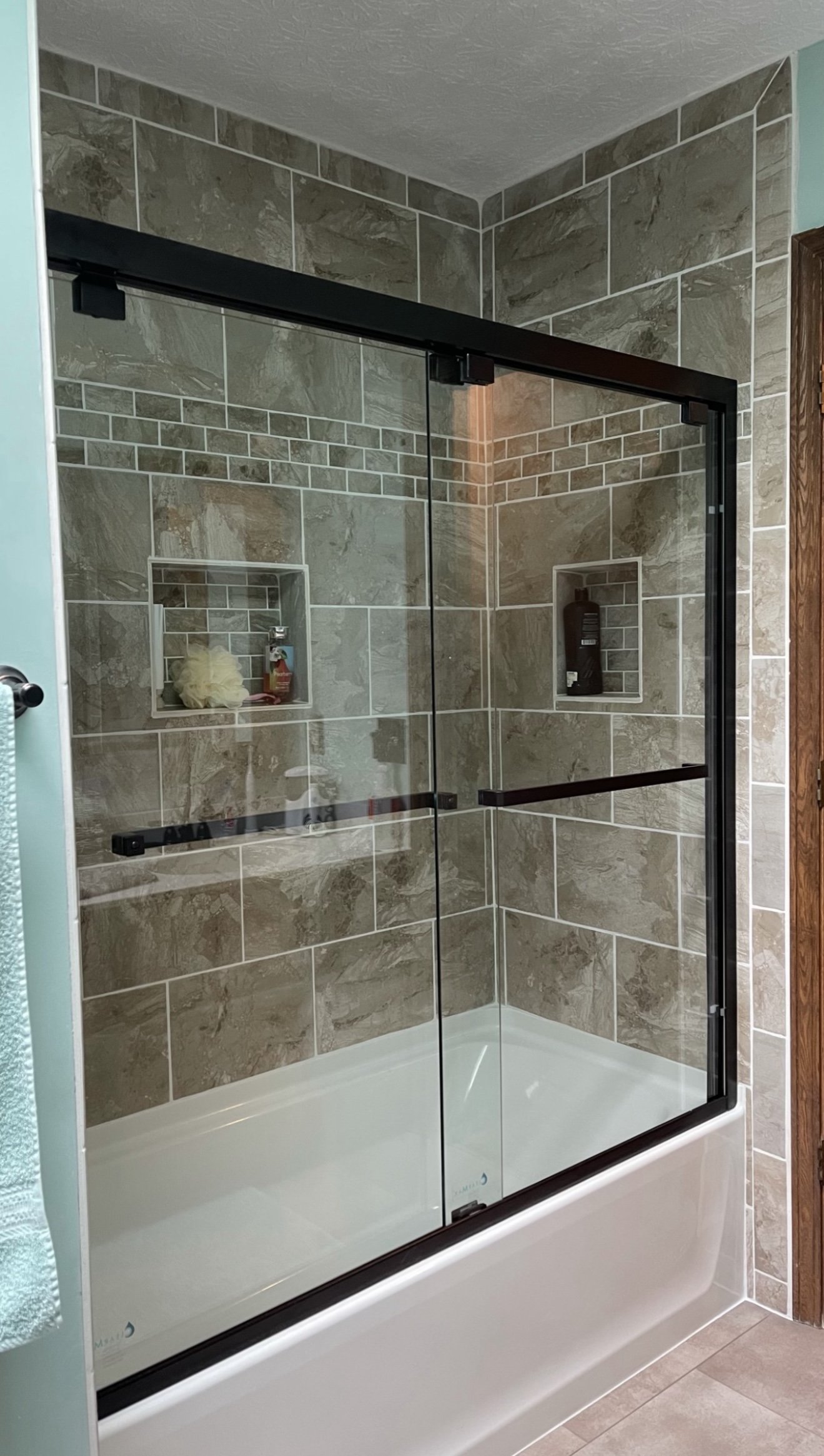 Modern bathroom with tiled shower and glass doors, featuring built-in shelves holding bath products.