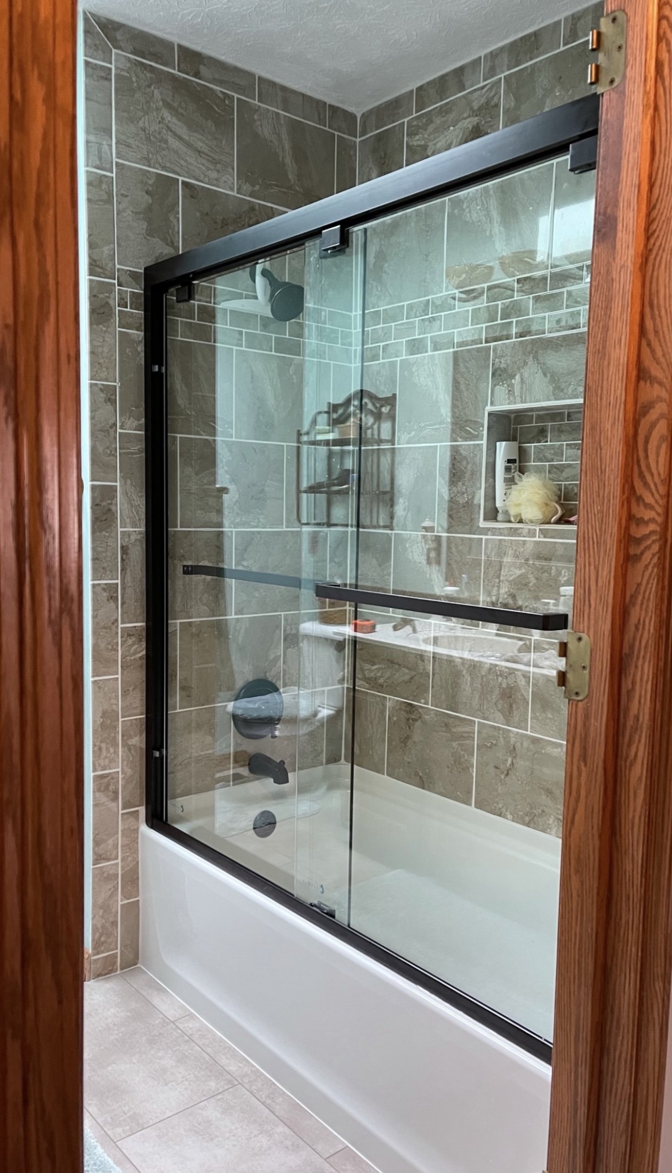 Modern bathroom with glass shower door, tiled walls, and built-in shelving.