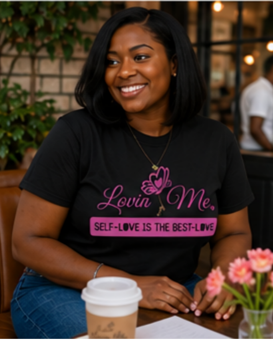 Message Wear image
Woman wearing a black “Self-Love Is the Best Love” T-shirt while seated at a café table.