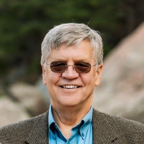 Dr. Leigh wearing sunglasses and a blazer, smiling outdoors.