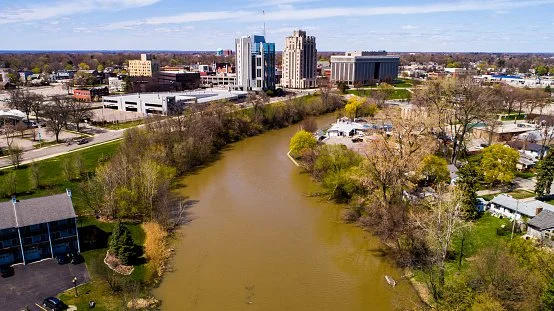 A cityscape with a river flowing through it, surrounded by trees and buildings in the background.