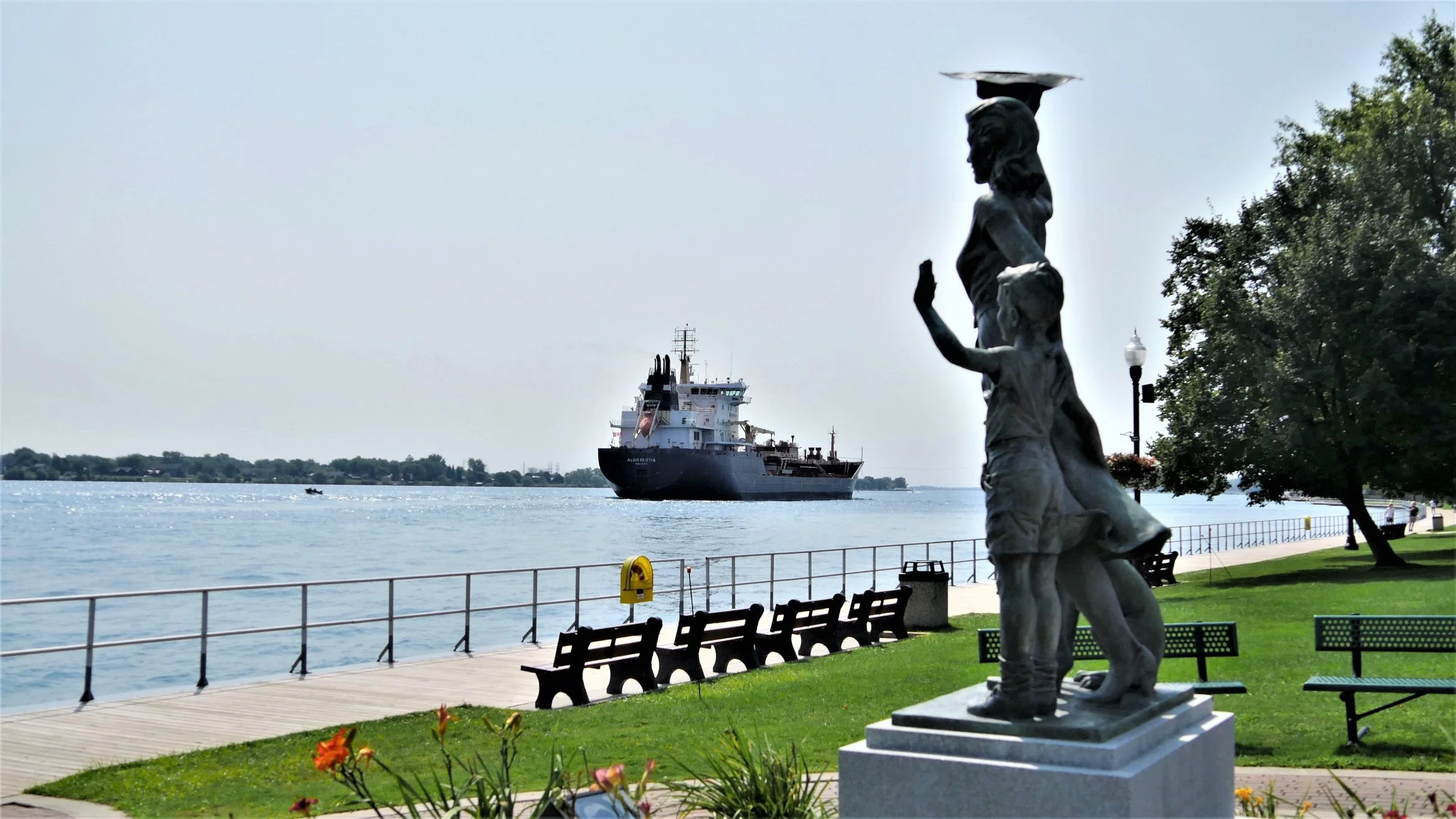 Statue of a woman with a child by the water with a ship in the background