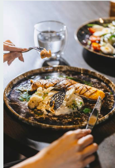 Person eating grilled salmon with vegetables and sauce