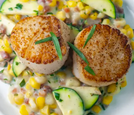 Seared scallops on a bed of creamy corn, zucchini, and bacon mixture