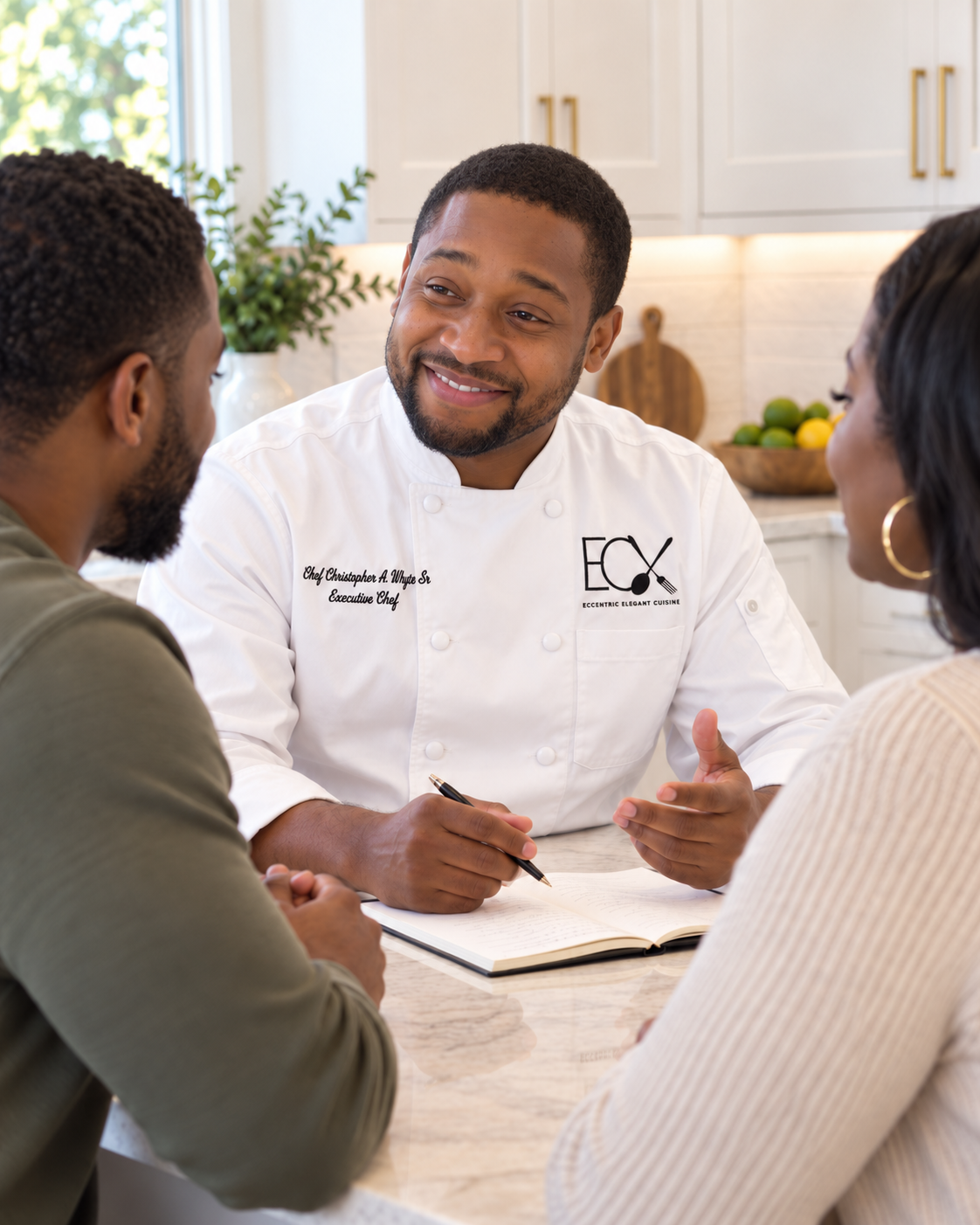 Chef Christopher A. White Sr. smiling and engaging with a couple sitting at a kitchen table during a consultation or meeting.