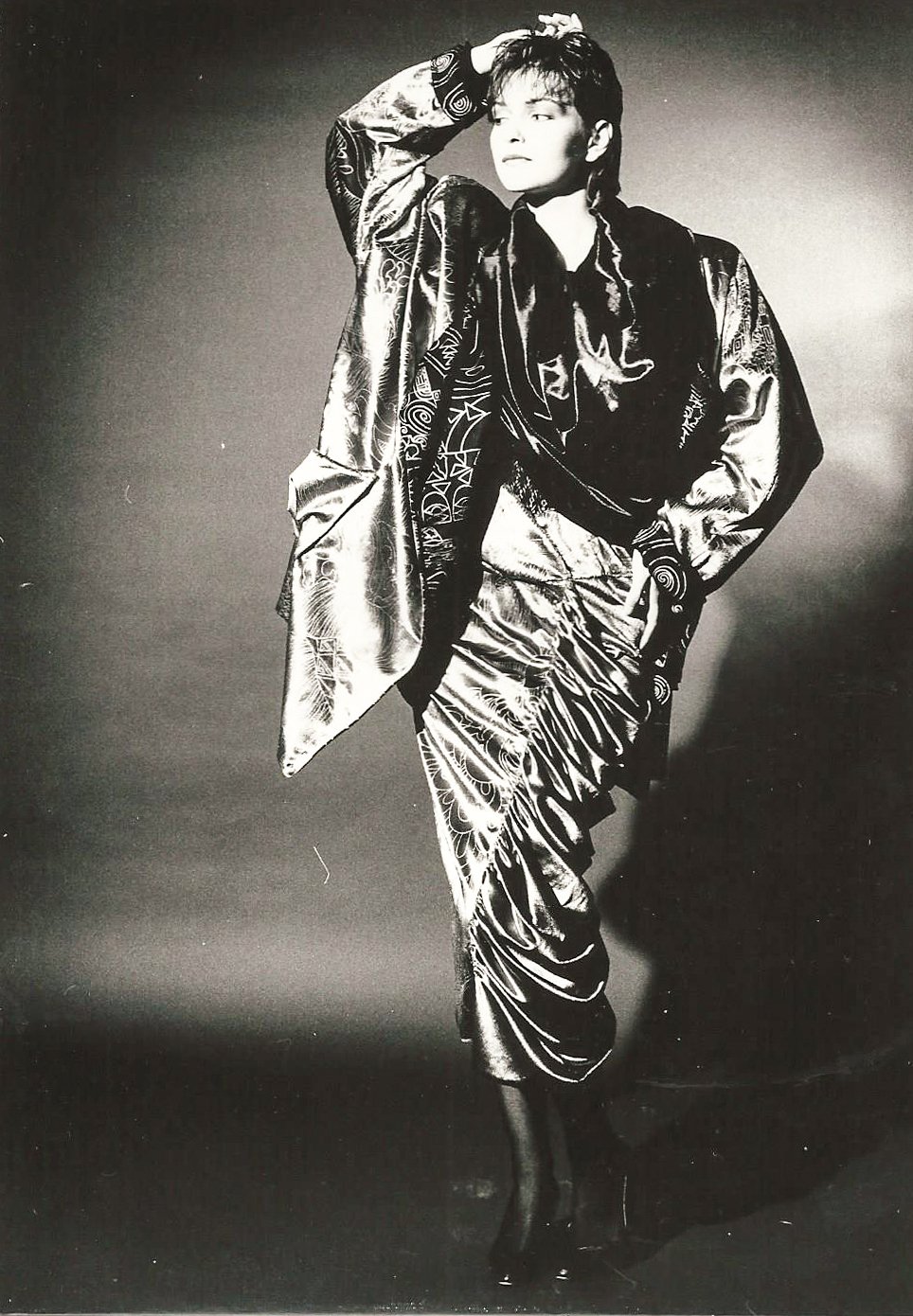 Schwarz-Weiß-Foto einer Person in einem stilvollen, glänzenden Outfit mit abstrakten Mustern.