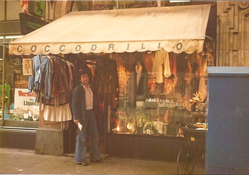 Vintage-Kleidungsgeschäft mit Schaufenster und markanter Markise. "COCCODRILLO" steht auf der Markise. Verschiedene Kleidungsstücke hängen draußen. Eine Person steht vor dem Geschäft.