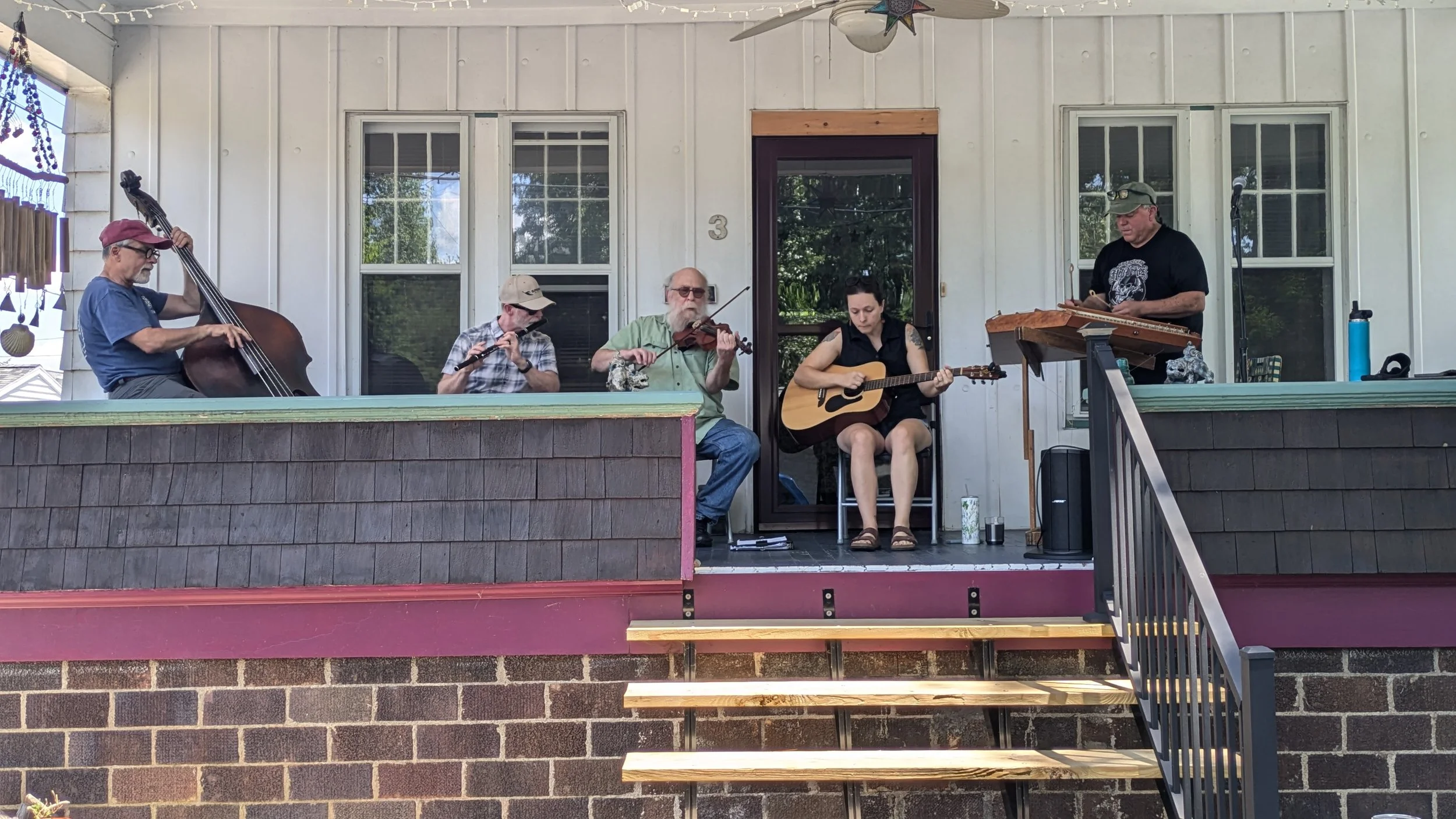 Five musicians playing a cello, flute, violin, guitar, and piano on a front porch during the 2024 Athens Porchfest.