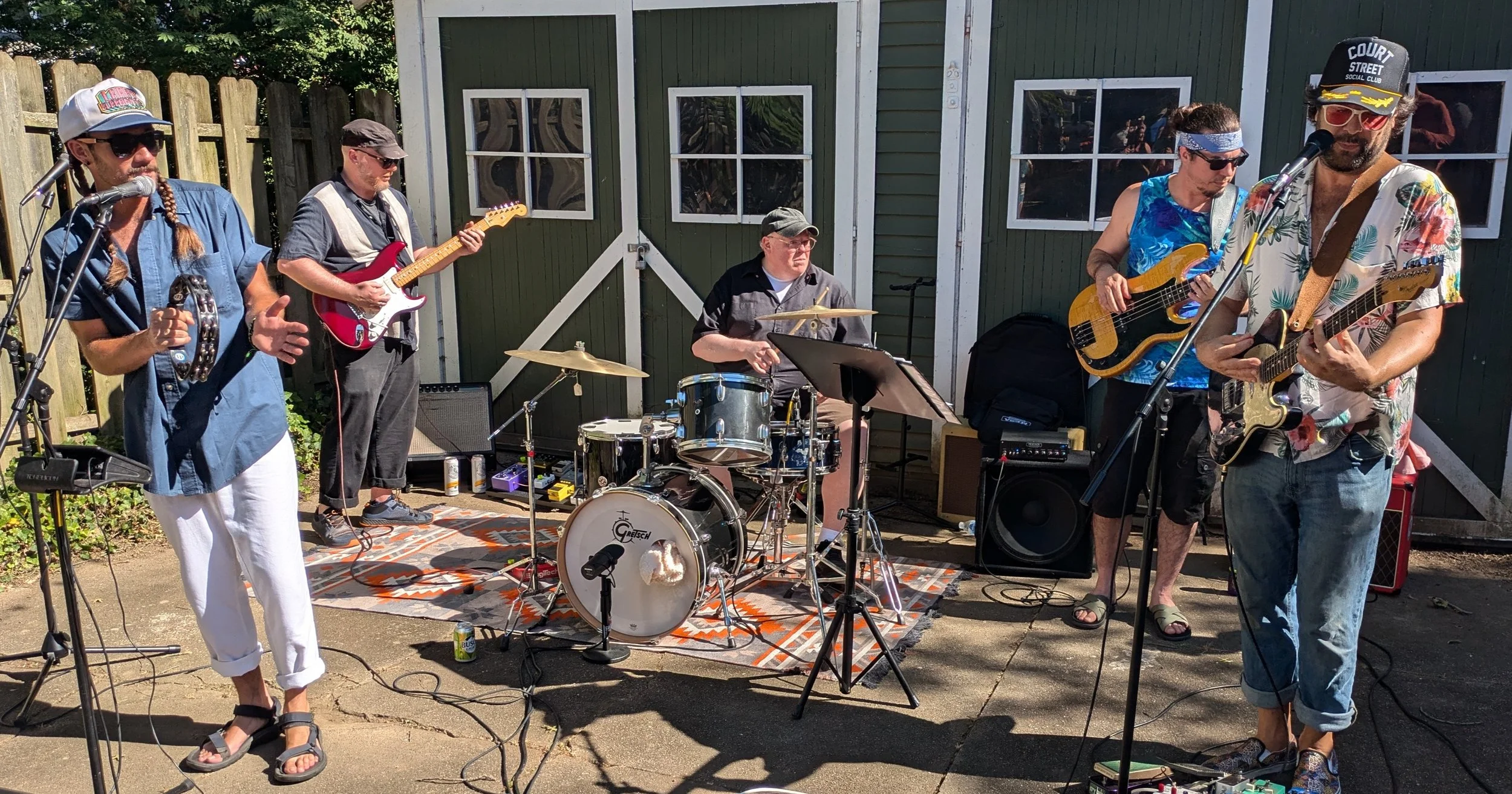 A band of five musicians playing various instruments in front of a large garage in a driveway during our 2024 Athens Porchfest.