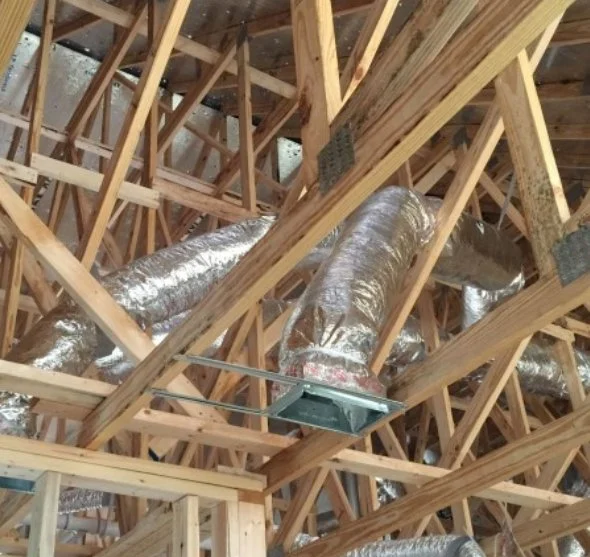 View of building's wooden framing with shiny silver HVAC ducts installed.