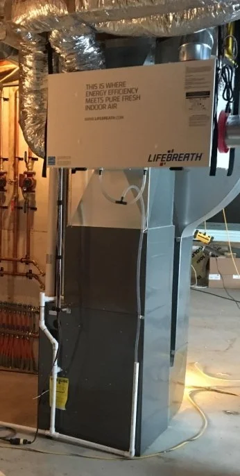 A LifeBreath indoor air purification system installed in a basement or utility room with various pipes and equipment in the background.