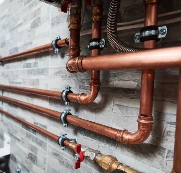 Copper plumbing pipes with valves and brackets mounted on a tiled wall.