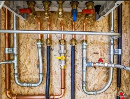 A wall with various copper, brass, and steel plumbing pipes connected with valves and fittings.