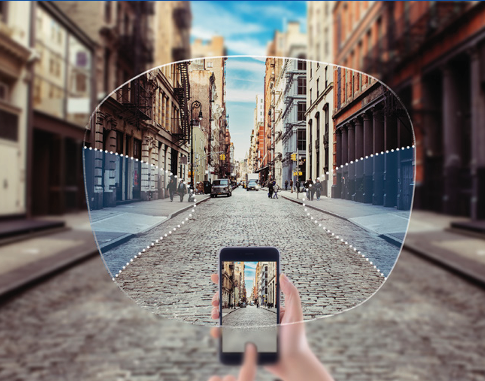 Hand holding a smartphone taking a photo of a city street with historic buildings, parked cars, and pedestrians on cobblestone pavement.