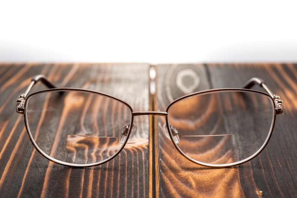 Close-up of a pair of eyeglasses resting on a wooden surface with a dark finish and visible wood grain patterns.