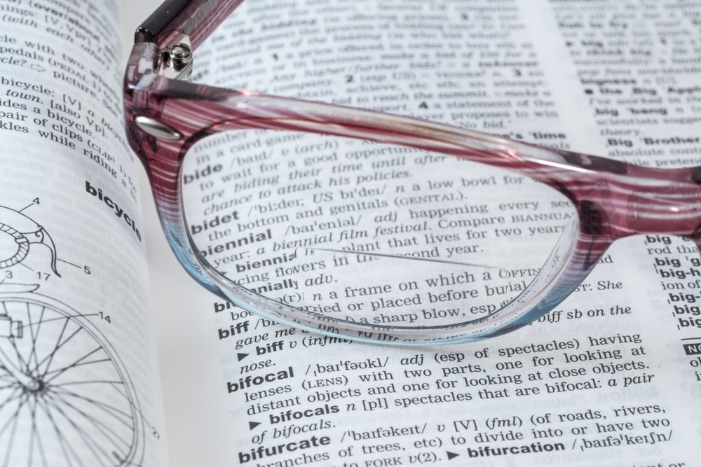 Close-up of a dictionary page with the word "bicycle" and a detailed bicycle diagram visible, accompanied by a pair of pink and clear glasses resting on the page.