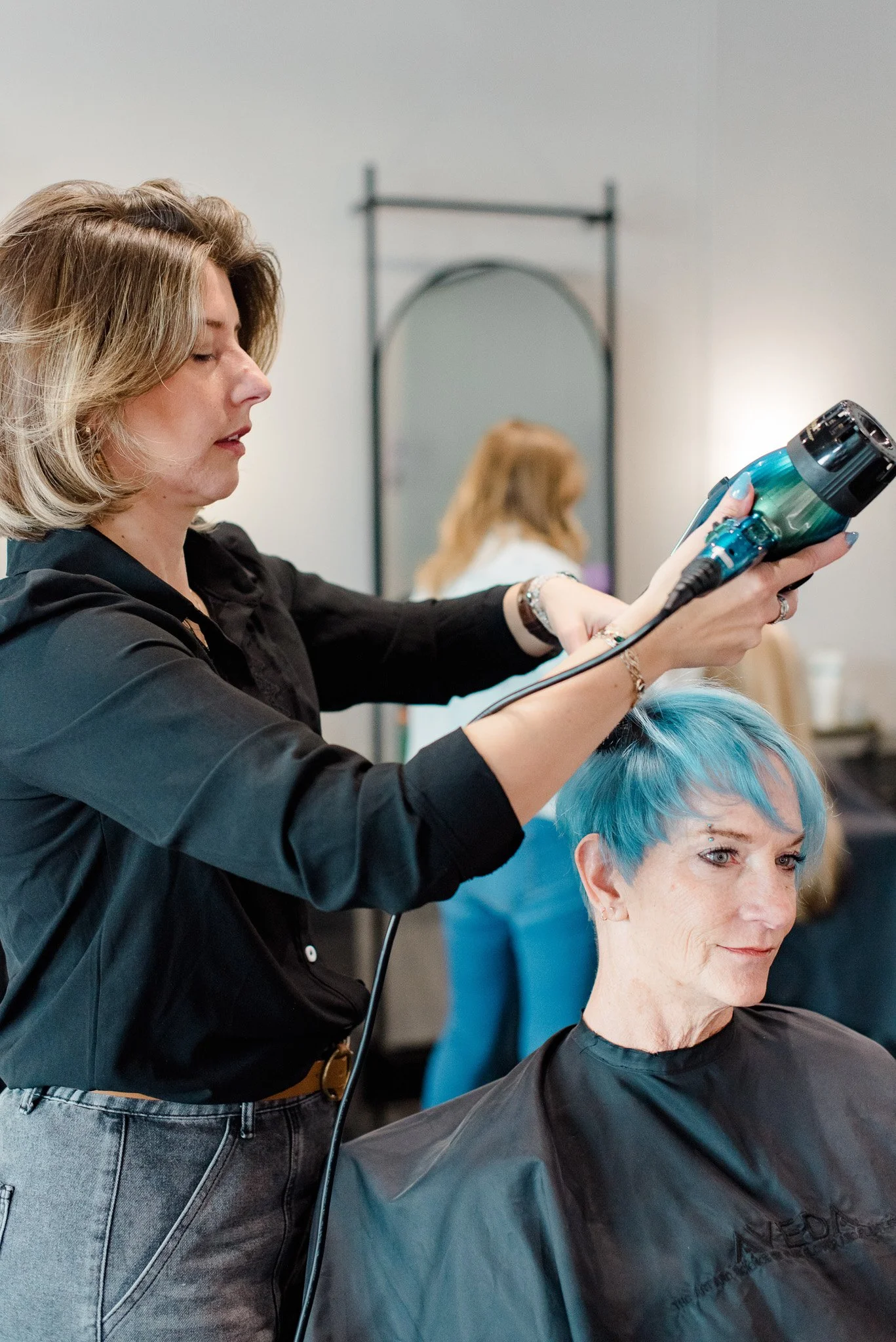 Experienced NoCo hair stylist blow drying a complex short haircut with vivid blue hair color.