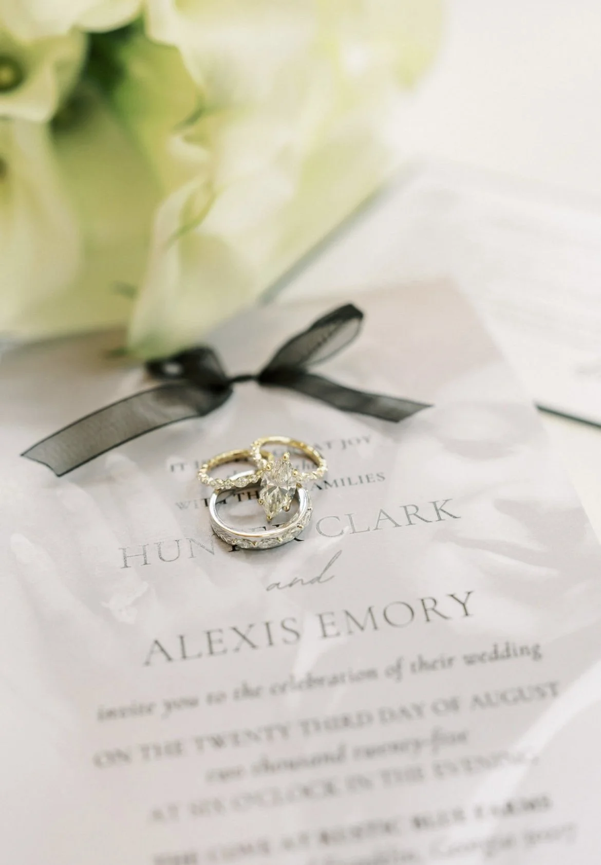 Close-up of wedding rings on wedding invitation with a bouquet in the background.