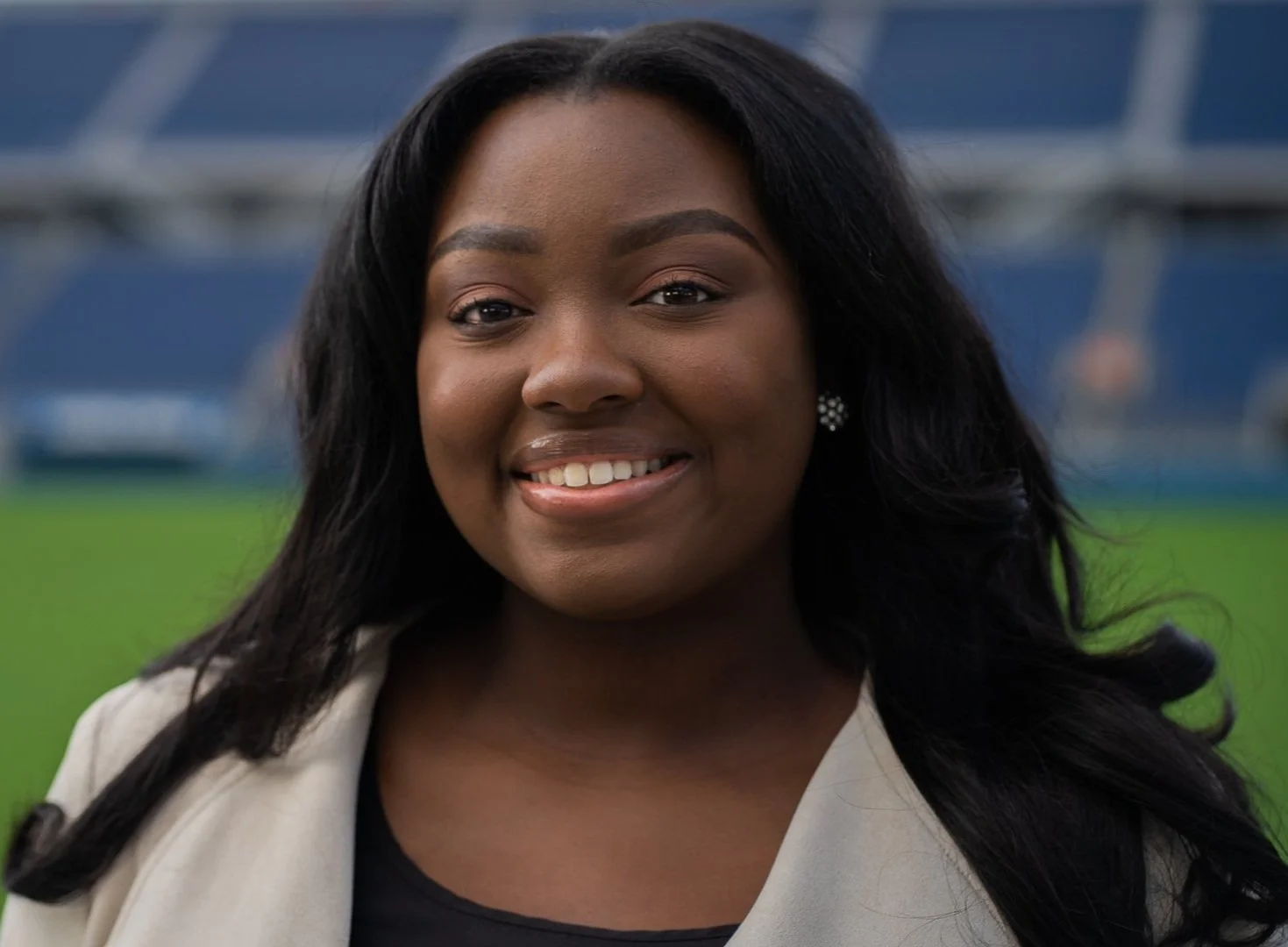 Smiling person with long hair in a stadium setting.