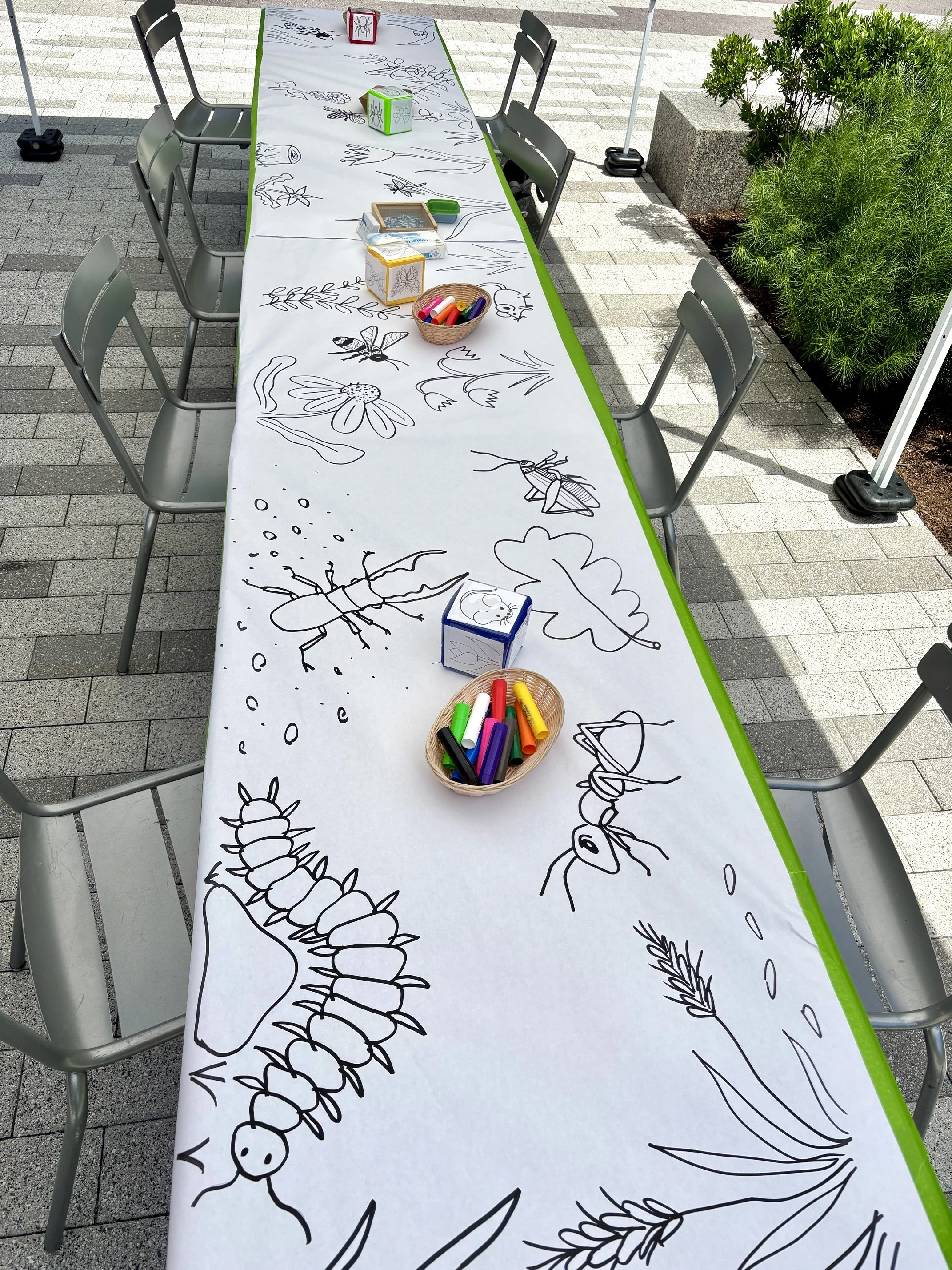 A large-scale community art project set up on a long table at a summer party