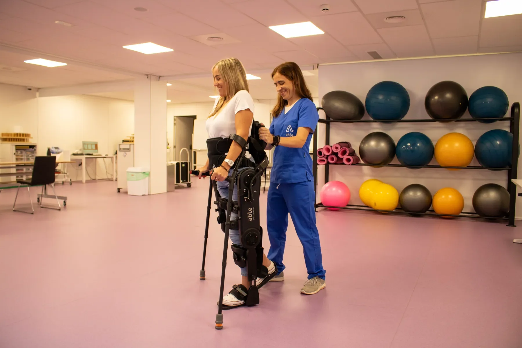 Paciente caminando con ABLE Exoskeleton durante sesión de neurorrehabilitación de la marcha con muletas en entorno clínico. Bayber