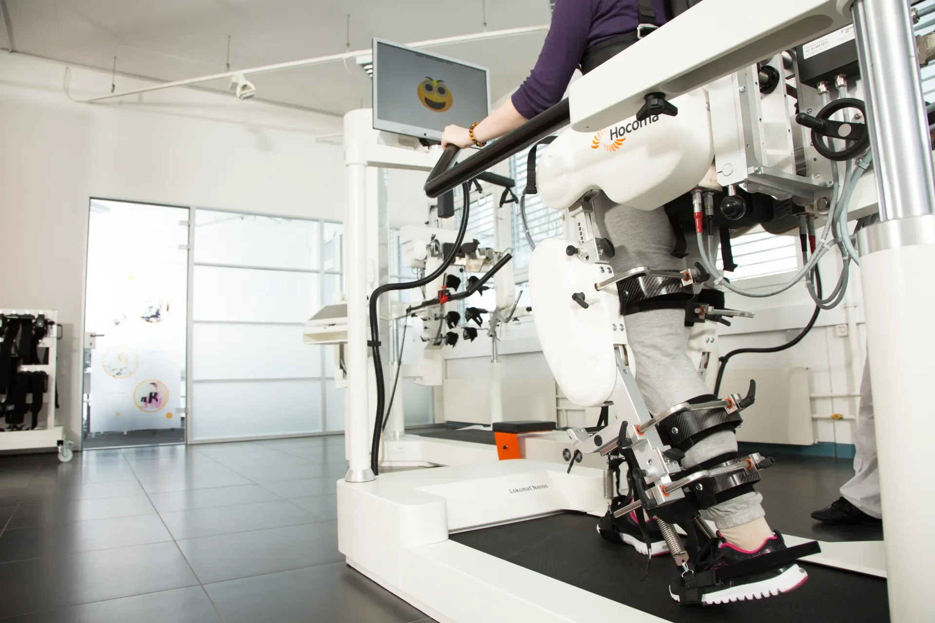 Paciente realizando terapia de marcha robotizada con Lokomat Nanos, con soporte parcial de peso y pantalla de feedback en sala de rehabilitación. Distribuido por Bayber en España y Portugal