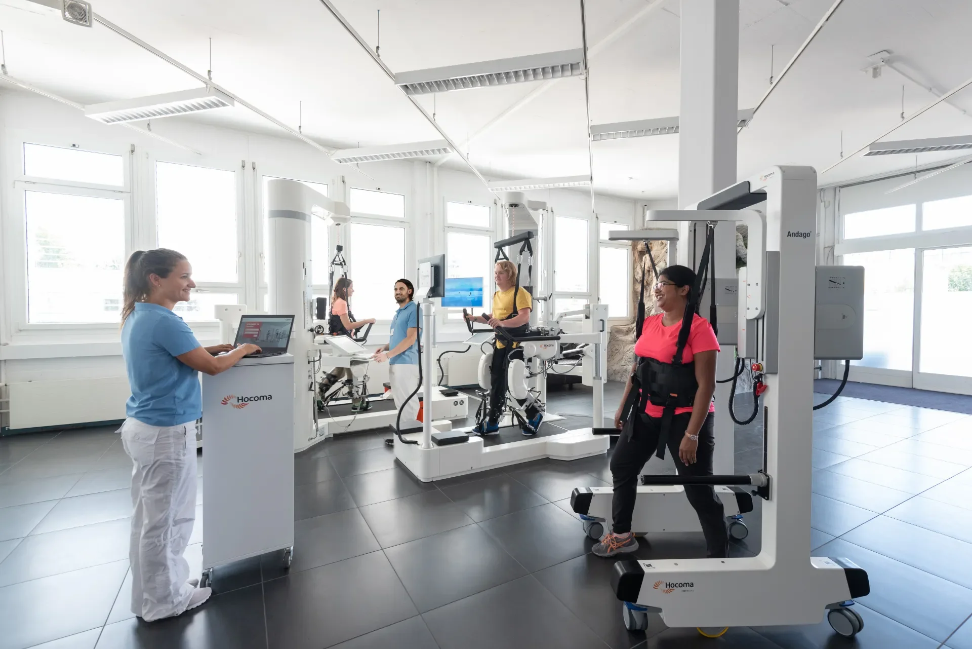 Sala de robótica clínica con varias unidades Andago 2.0 y pacientes en rehabilitación de la marcha supervisada por profesionales. Bayber distribuye Andago en España y Portugal
