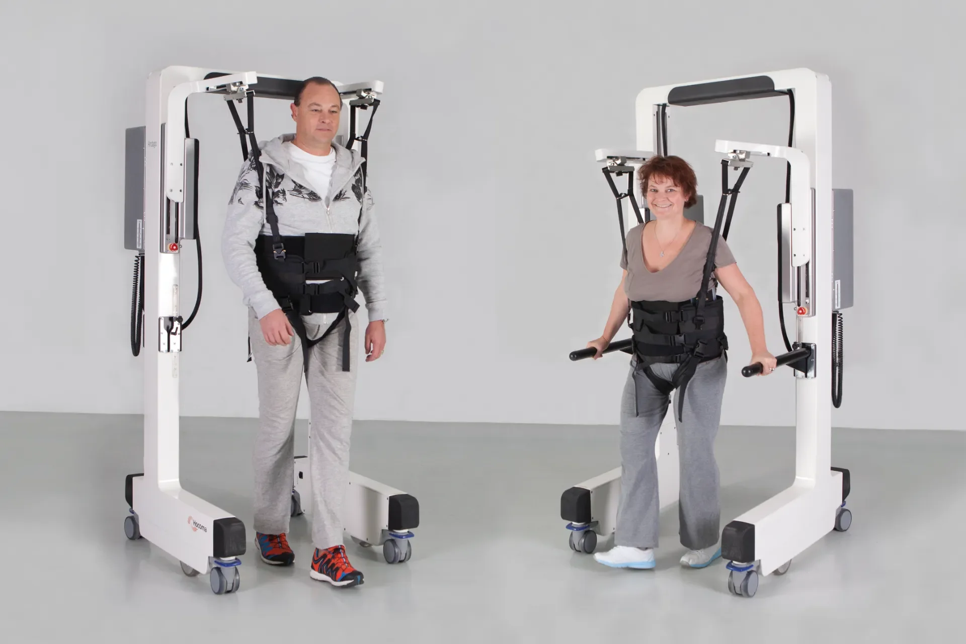 Dos pacientes adultos realizando rehabilitación de la marcha con Andago 2.0, con movilidad asistida mediante arnés de soporte de peso corporal.