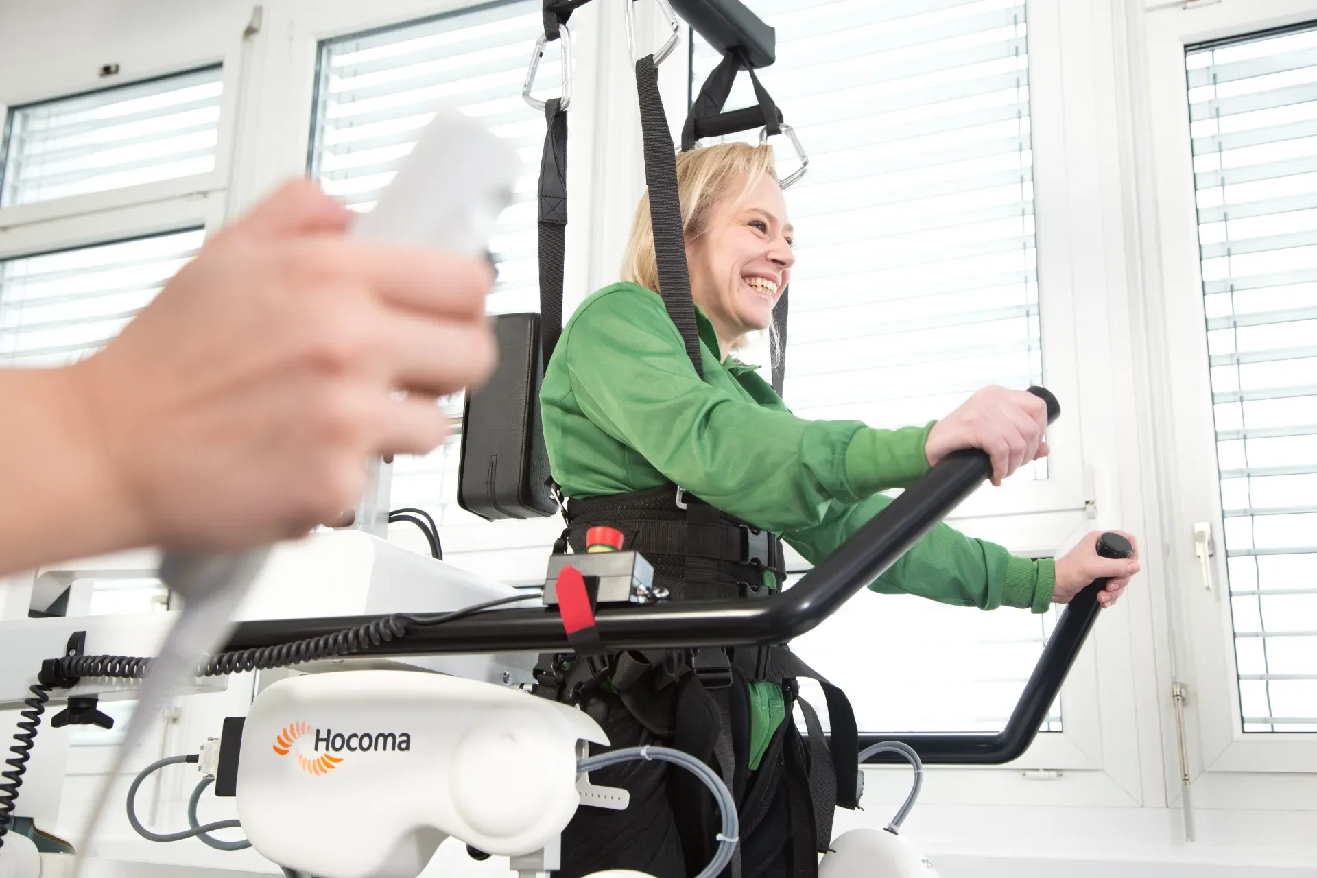 Primer plano de paciente en Lokomat Pro sujetando las barras mientras el profesional controla la marcha asistida por robot con un mando. Bayber distribuidor oficial de Hocoma en España y Portugal