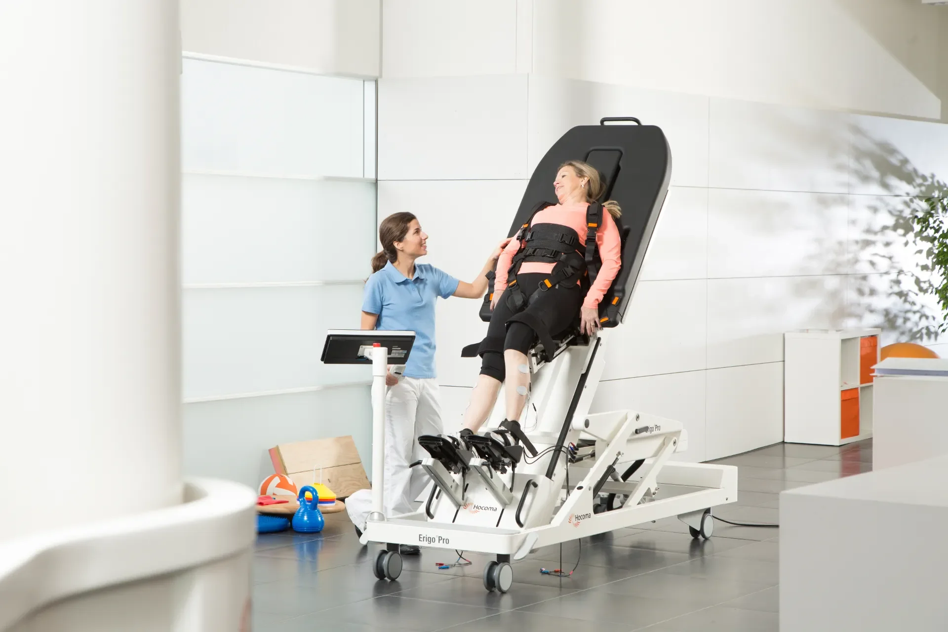 Profesional de rehabilitación neurológica usando Erigo Pro como mesa de bipedestación para entrenamiento de marcha precoz. Distribuido en España por Bayber Health