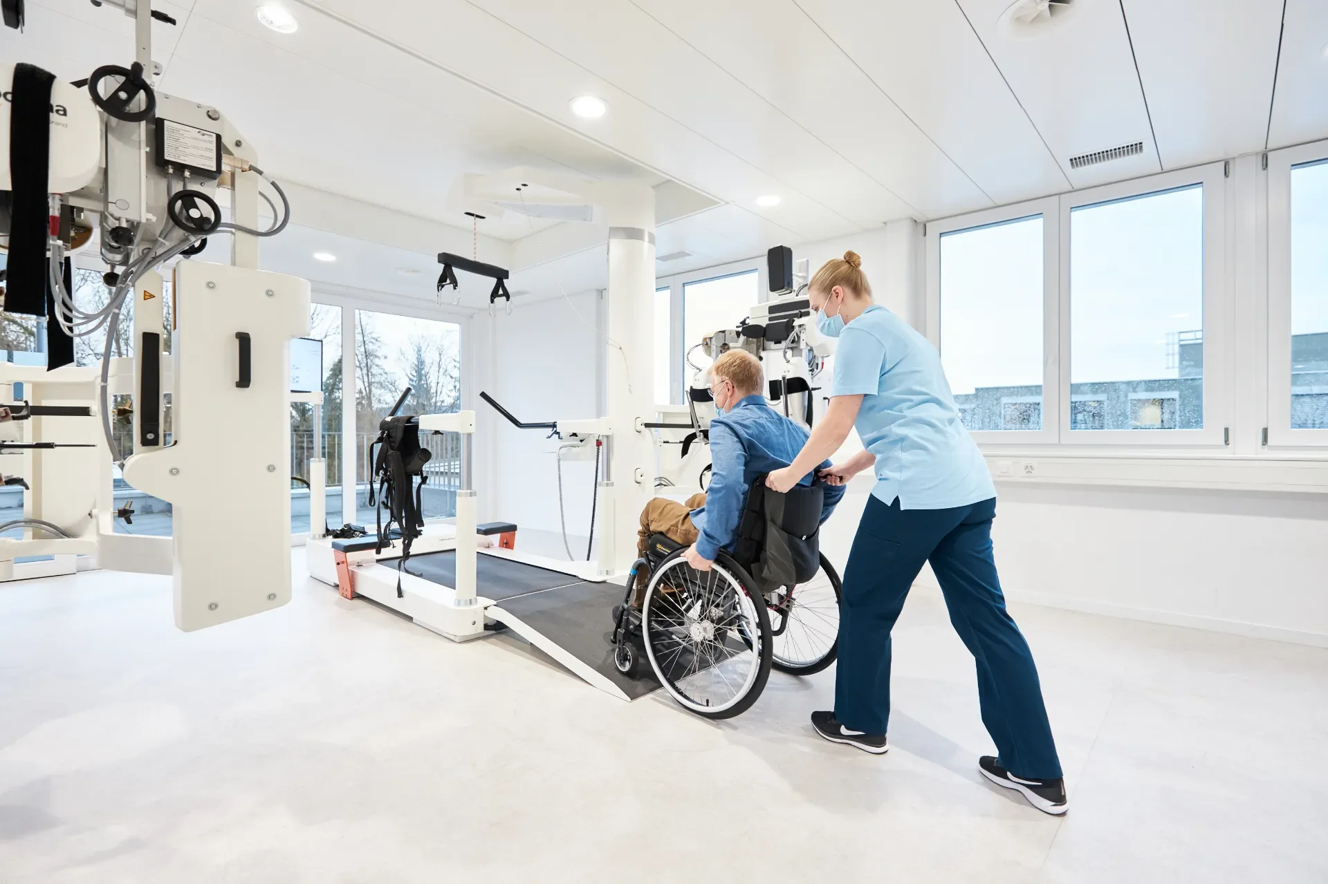 Profesional sanitario acercando a un paciente en silla de ruedas al sistema Lokomat Nanos para inicio de rehabilitación de marcha tras ictus o lesión medular. Distribuido por Bayber en España y Portugal