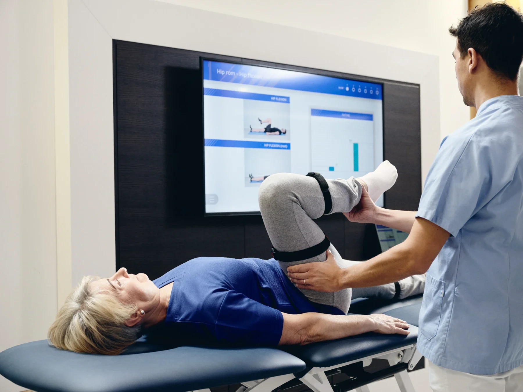 Fisioterapeuta movilizando la cadera de una paciente en camilla con sensor Euleria Lab en el muslo y registro del rango de movimiento en pantalla