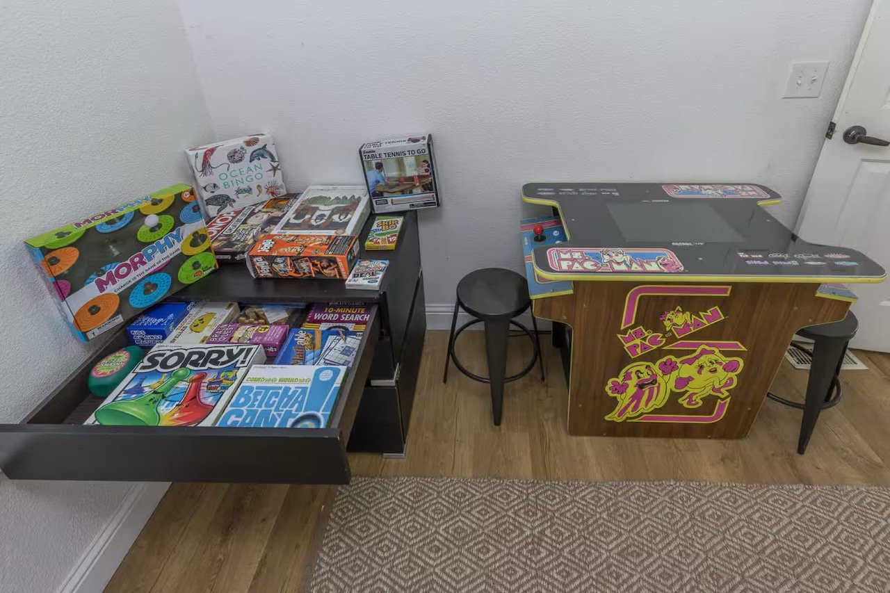 Room with a Ms. Pac-Man arcade machine and shelves filled with various board games including Sorry and Ocean Bingo.