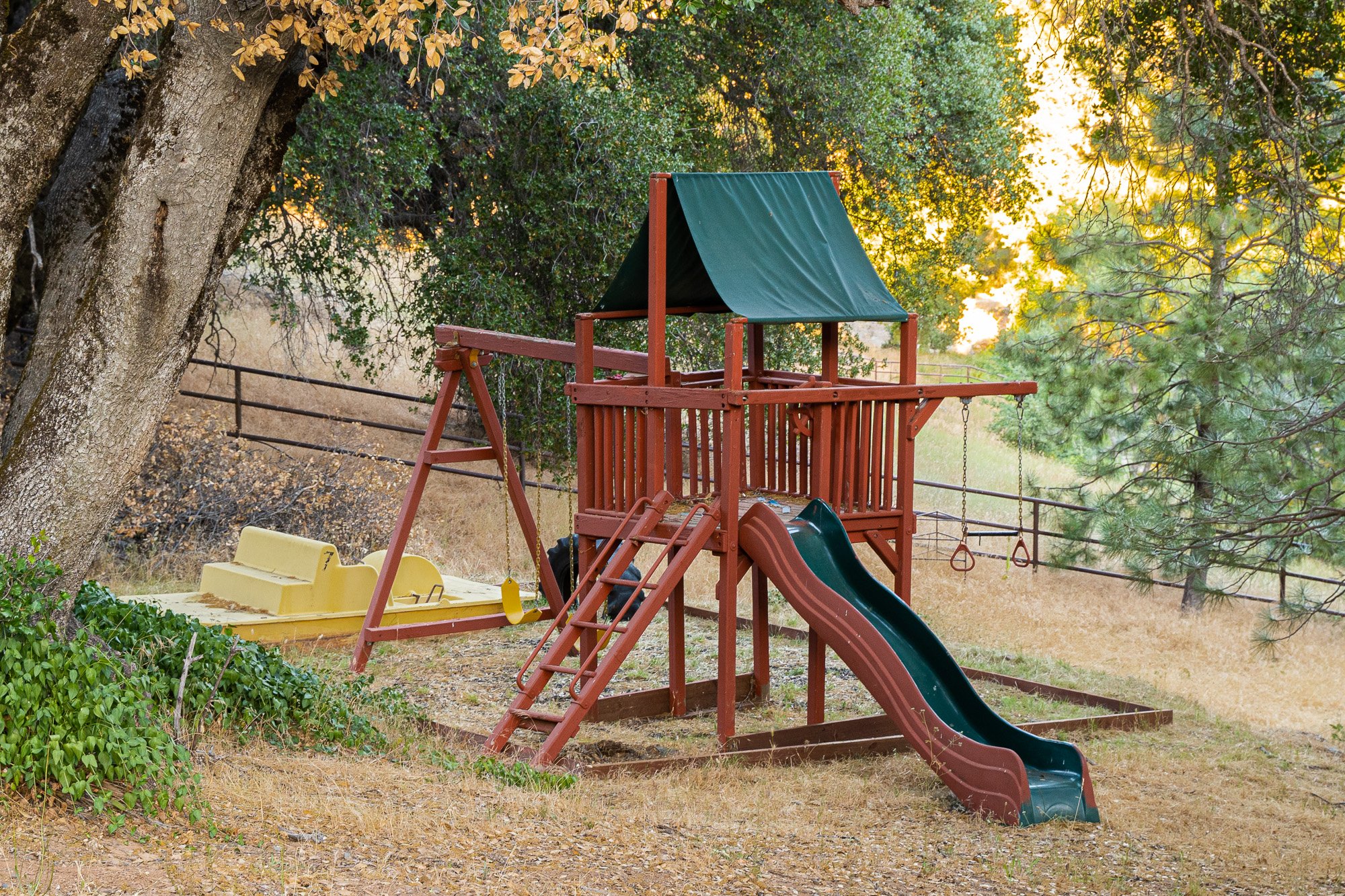 Wooden playset with slide and swings in a backyard surrounded by trees.