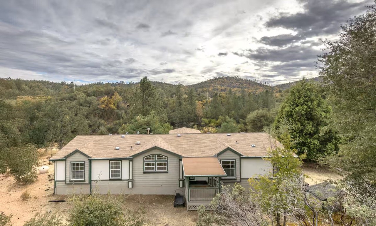 Ranch-style house in a forested area with cloudy sky