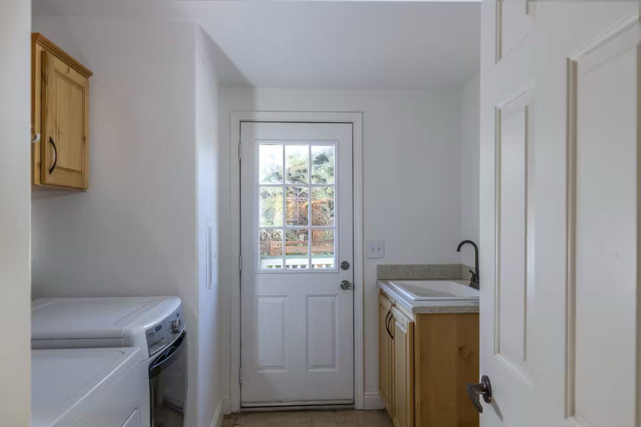Small laundry room with washing machine, wooden cabinets, sink, and glass-panel door.