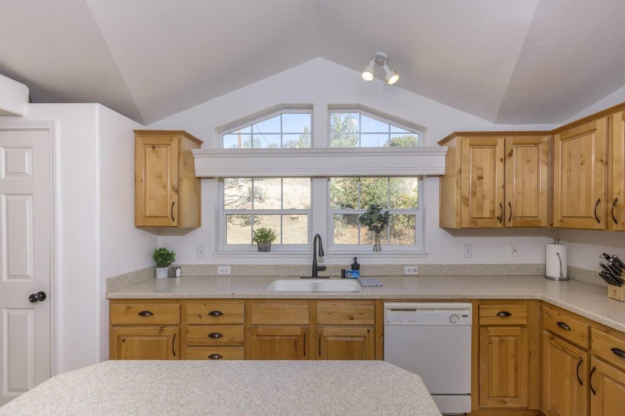 kitchen with wooden cabinets and counter, large windows, sink, dishwasher, and plants