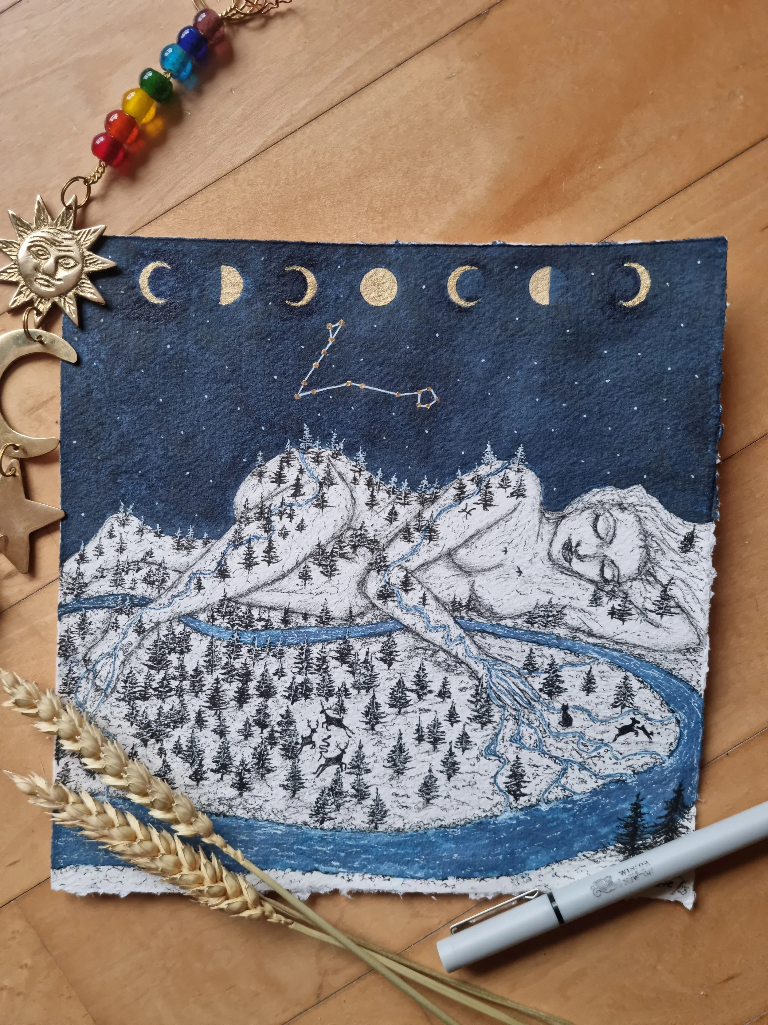 A cloth art piece depicting a mountainous landscape with a river, trees, and a sleeping figure to the right. The night sky above features moons at different phases and a constellation of stars forming the letter 'Z'.