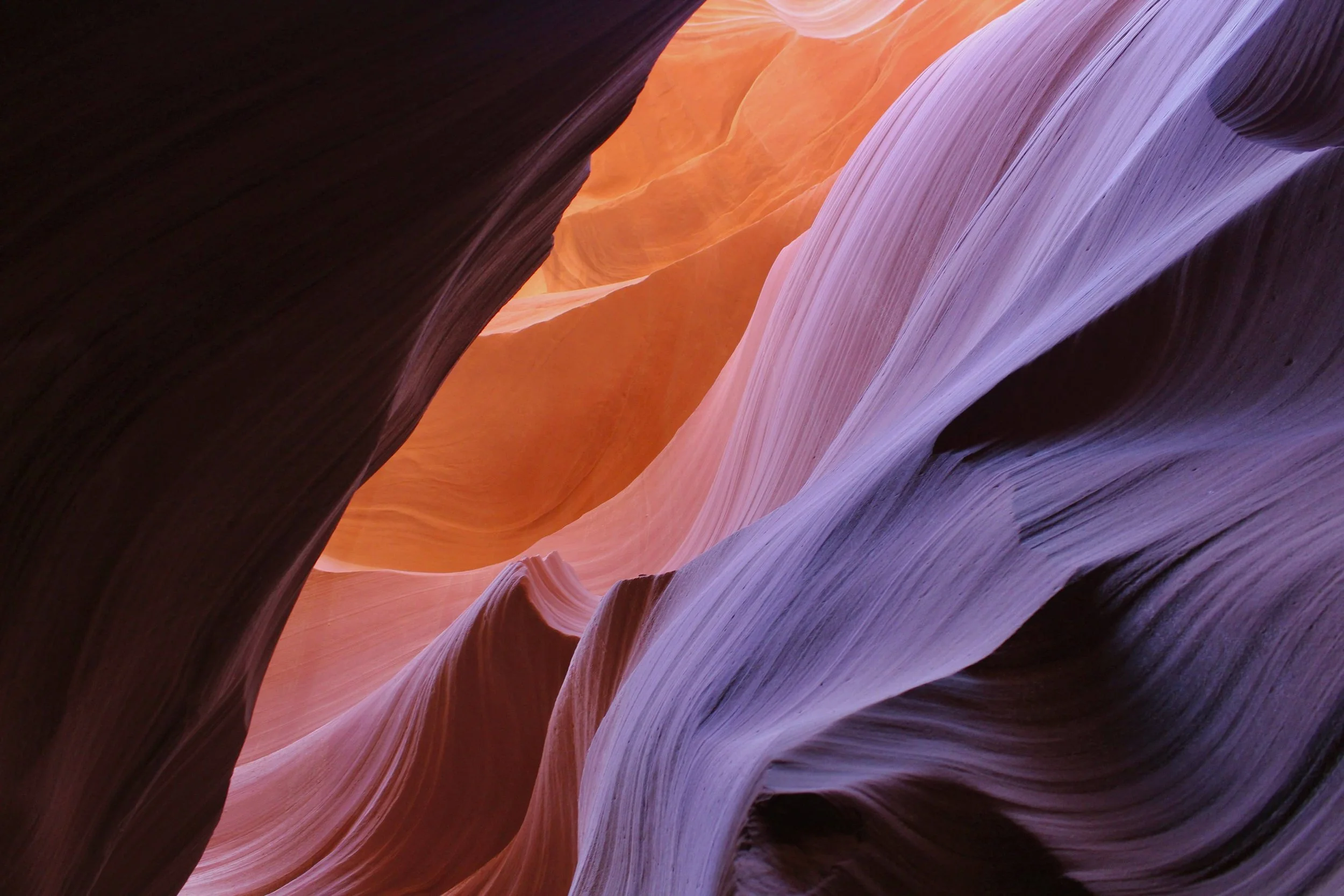 Narrow slot canyon with smooth, layered sandstone walls in shades of purple, pink, orange, and dark brown.