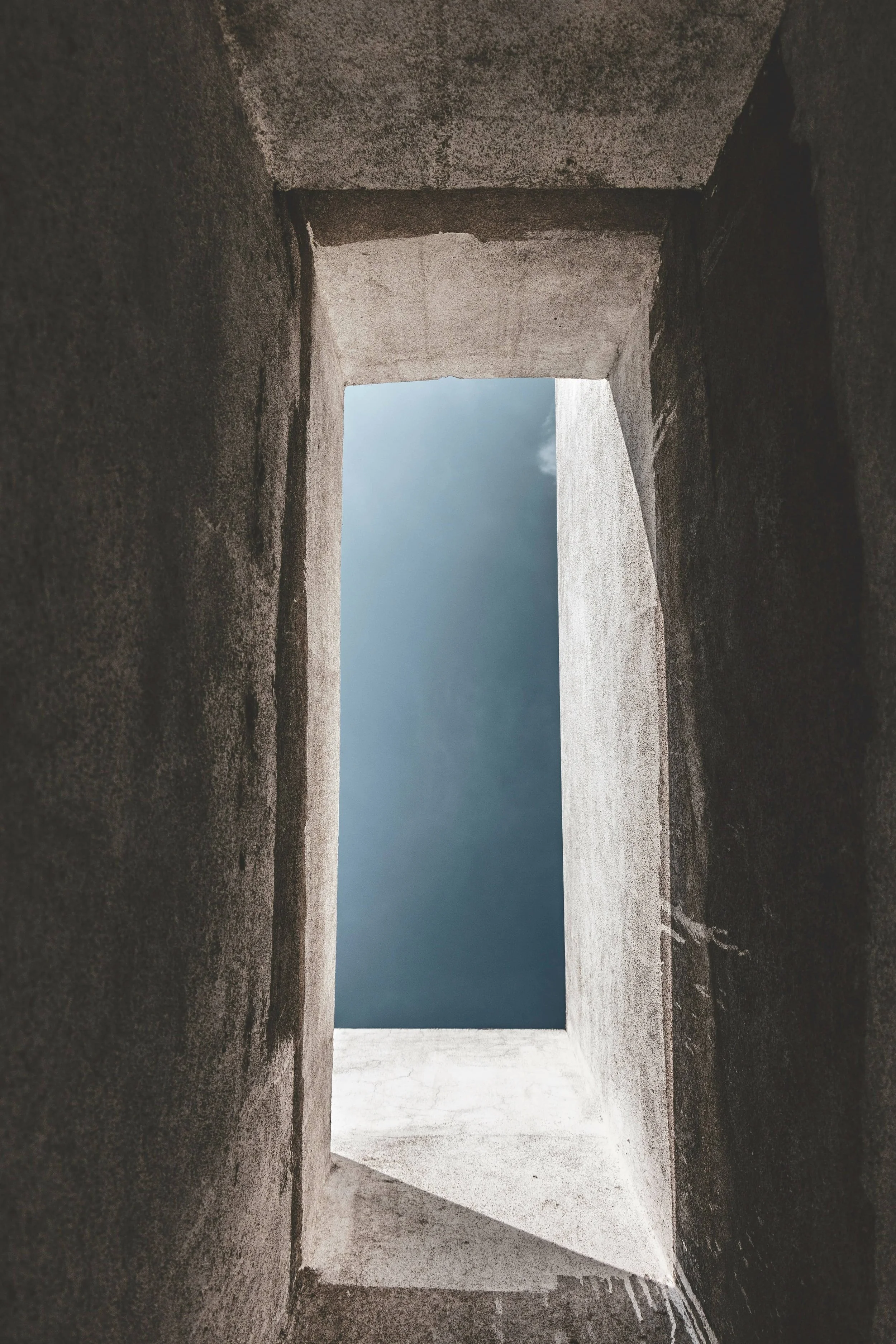 View through a rectangular opening in a stone or concrete wall, showing a cloudy sky outside.