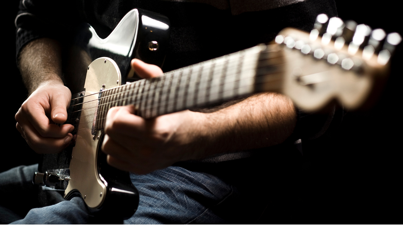 Close-up of a person playing a black electric guitar.