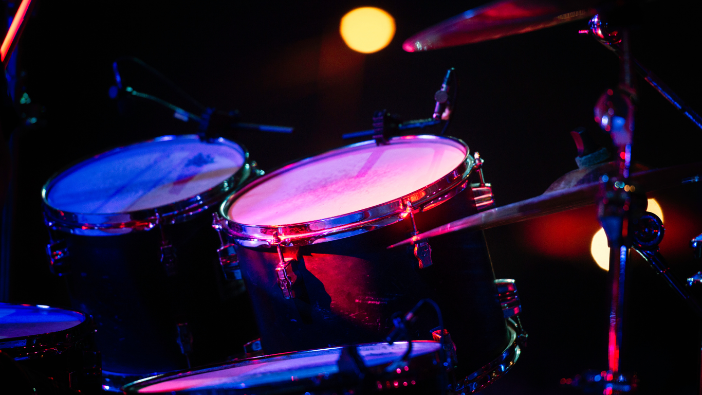 Close-up of a drum set under colorful stage lights with microphones positioned nearby.