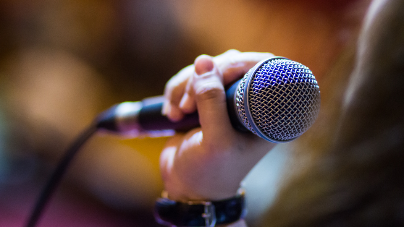 Close-up of a person holding a microphone with a soft-focus background.