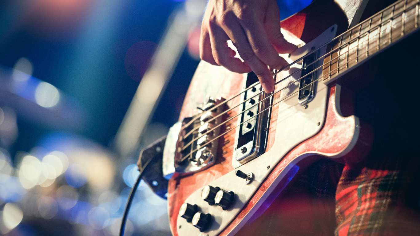 Close-up of a person playing a red electric bass guitar on stage.