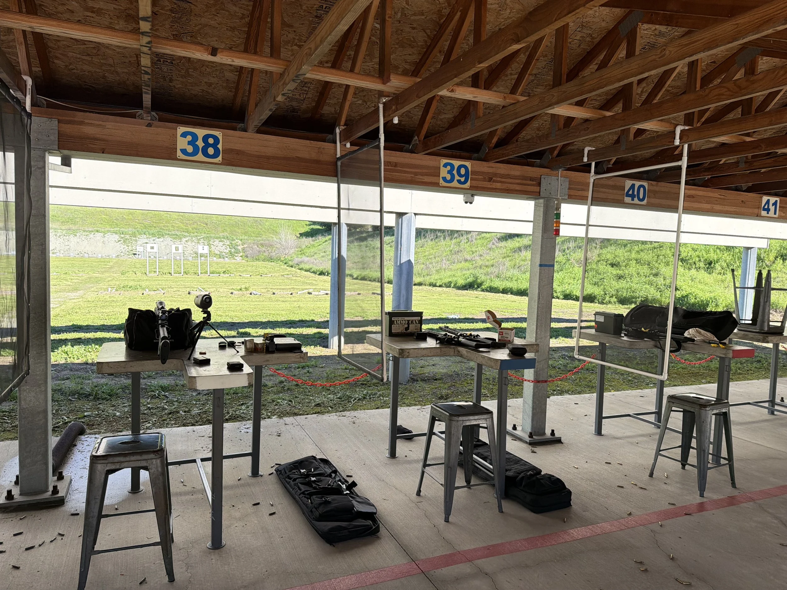Shooting range with numbered lanes sectioned off with signs 38 to 41, target stands in the background, and shooting equipment on tables and on the ground.