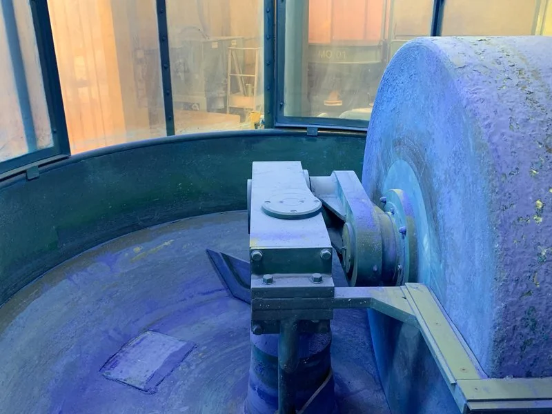 Close-up of a large circular industrial grinding or polishing machine with a rotating abrasive wheel inside an enclosed workspace.