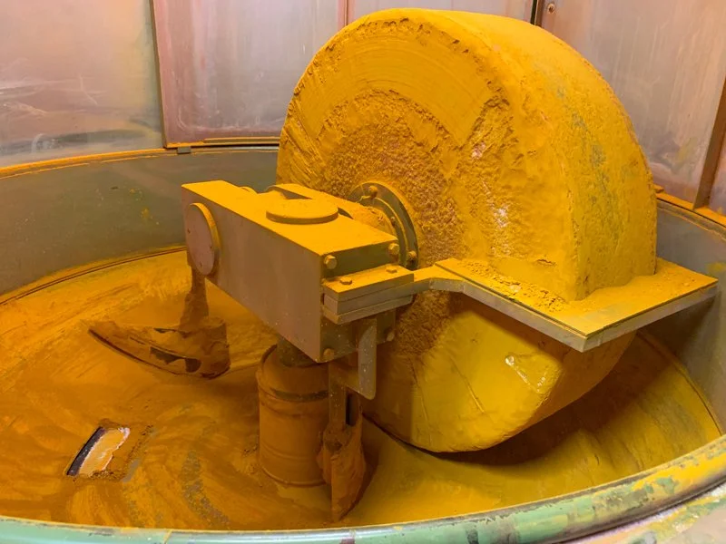 A large industrial circular saw cutting through a thick, yellowish-brown material, likely wood or a similar substance.