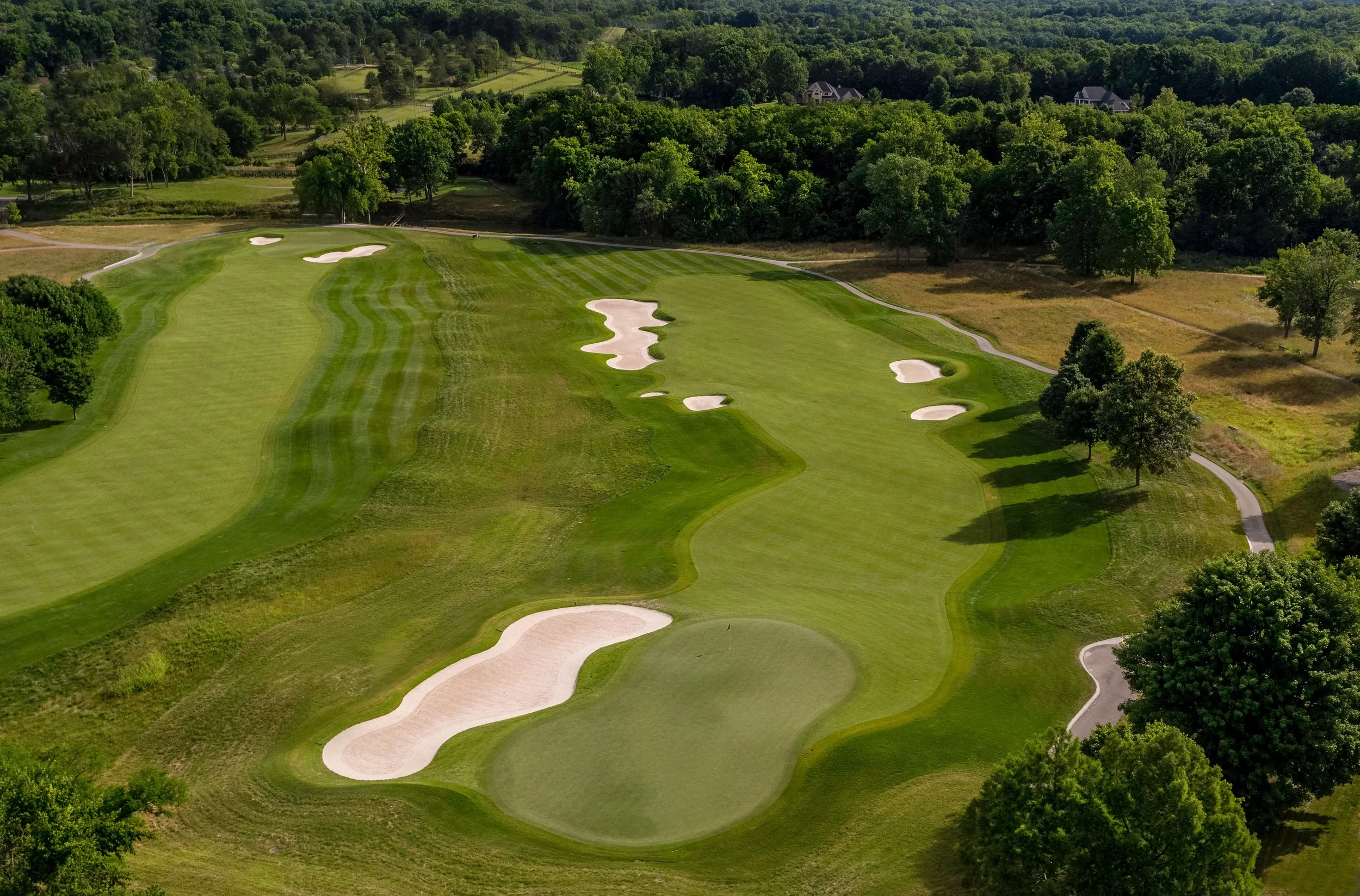 Aerial view of a golf course with multiple sand bunkers, green fairways, and trees surrounding the area.